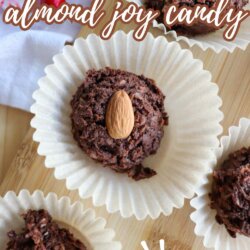 Close-up of chocolate almond candy clusters on white paper wrappers, each topped with a whole almond, displayed on a wooden surface with text: Crockpot almond joy candy, so easy.