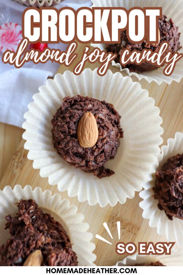Close-up of chocolate almond candy clusters on white paper wrappers, each topped with a whole almond, displayed on a wooden surface with text: Crockpot almond joy candy, so easy.