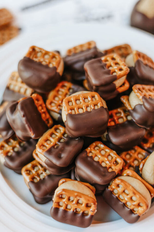 A plate piled with sandwich-style treats made of pretzels and a filling, half-dipped in chocolate.