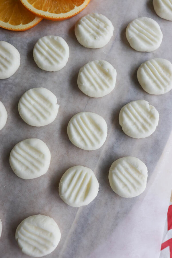 Round white mints with fork marks on top are arranged in rows on parchment paper, with orange slices partially visible in the corner.