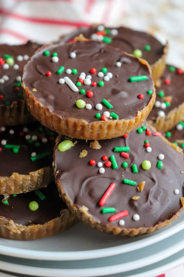A stack of chocolate-topped peanut butter cups decorated with red, white, and green sprinkles, arranged on a white plate.