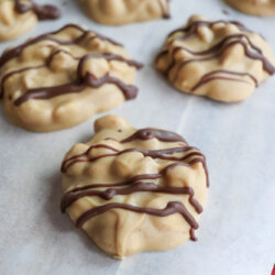 Clusters of peanut butter and chocolate candy are arranged on a sheet of parchment paper, each drizzled with chocolate on top.