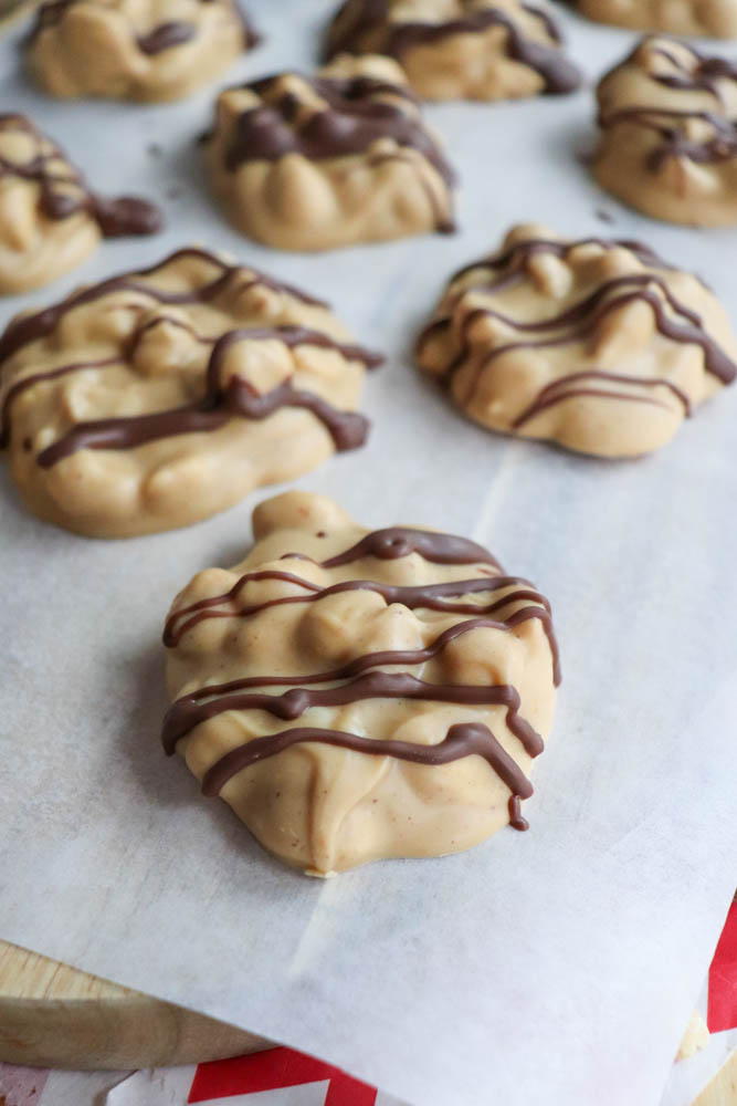 Clusters of peanut butter and chocolate candy are arranged on a sheet of parchment paper, each drizzled with chocolate on top.