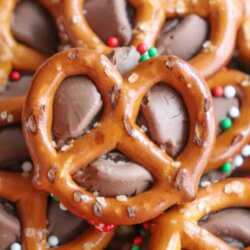 A close-up of pretzel bites topped with melted chocolate and festive red, green, and white sprinkles. Text reads “ROLO PRETZEL bites” and “HOMEMADEHEATHER.COM.”.