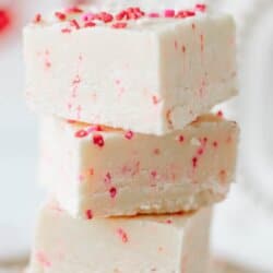 Four pieces of white fudge with pink and red sprinkles are stacked on top of each other. The text reads “Valentine’s Day fudge recipe” and “homemadeheather.com.”.