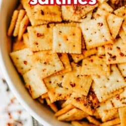 A bowl filled with seasoned saltine crackers topped with red pepper flakes. Bold red text at the top reads firecracker saltines. The bottom of the image displays the website homemadeheather.com.