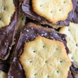 A close-up of homemade toffee topped with a layer of melted chocolate and Ritz crackers, stacked together on a plate. Text on the image reads Ritz Cracker Toffee and homemadeheather.com.