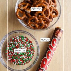 A bowl of pretzels, a bowl of red, white, and green sprinkles, and a roll of Rolo chocolates are arranged on a light wooden surface. Each item is labeled with text.