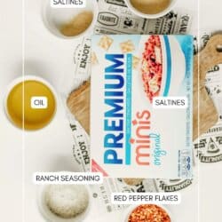 A box of Premium Minis saltine crackers on a table surrounded by bowls labeled as saltines, oil, ranch seasoning, and red pepper flakes. The website homemadheather.com is at the bottom.