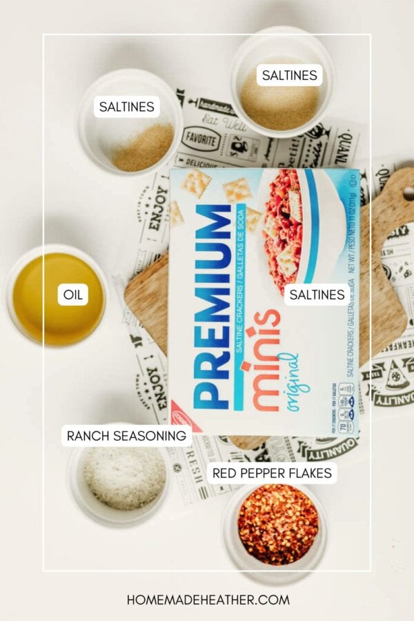 A box of Premium Minis saltine crackers on a table surrounded by bowls labeled as saltines, oil, ranch seasoning, and red pepper flakes. The website homemadheather.com is at the bottom.