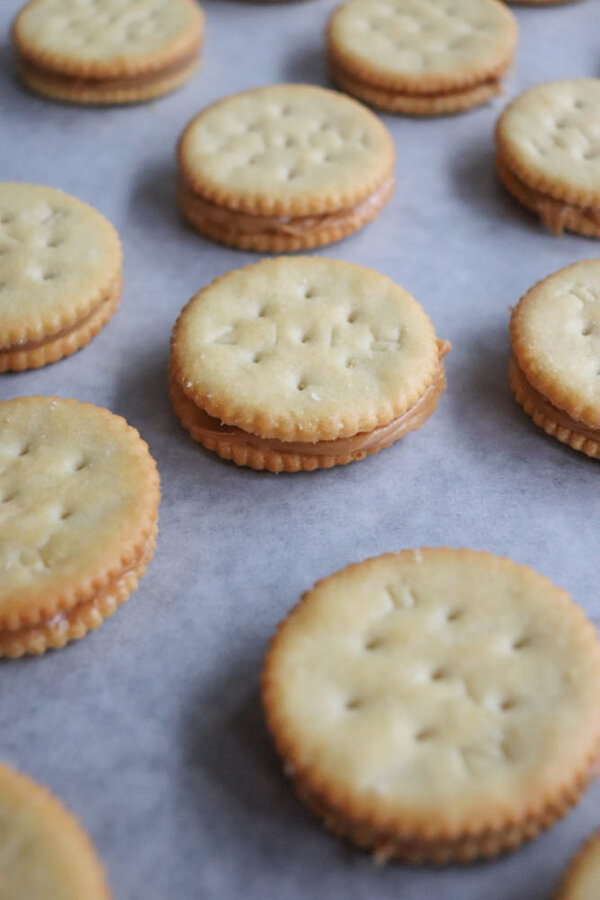 Sandwich crackers with a peanut butter filling are arranged in rows on a sheet of parchment paper.