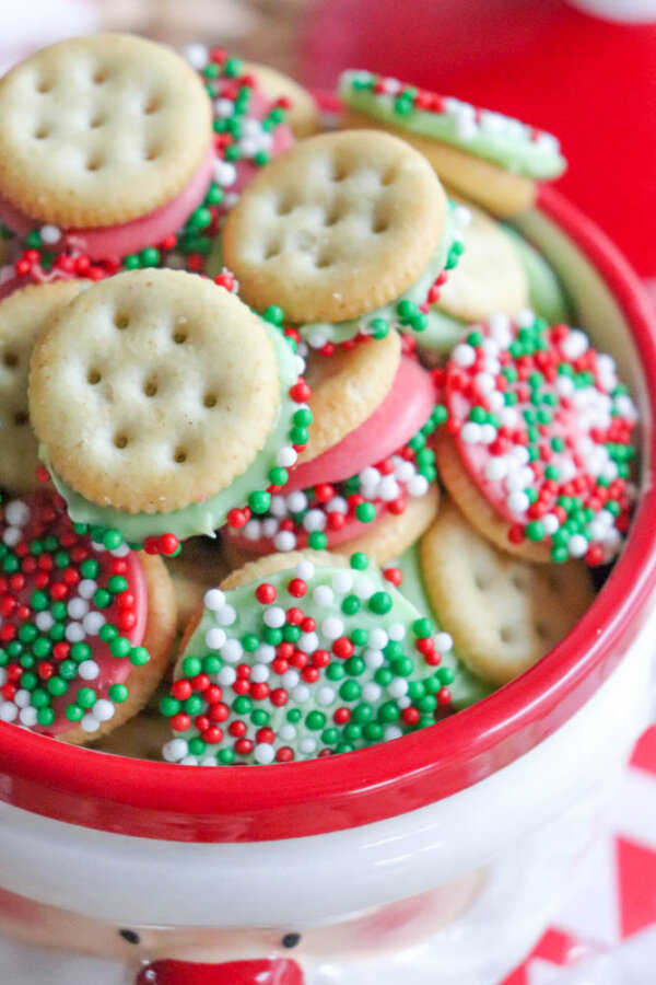 A bowl filled with sandwich cookies, some dipped in chocolate and coated with red, white, and green sprinkles, creating a festive holiday look.