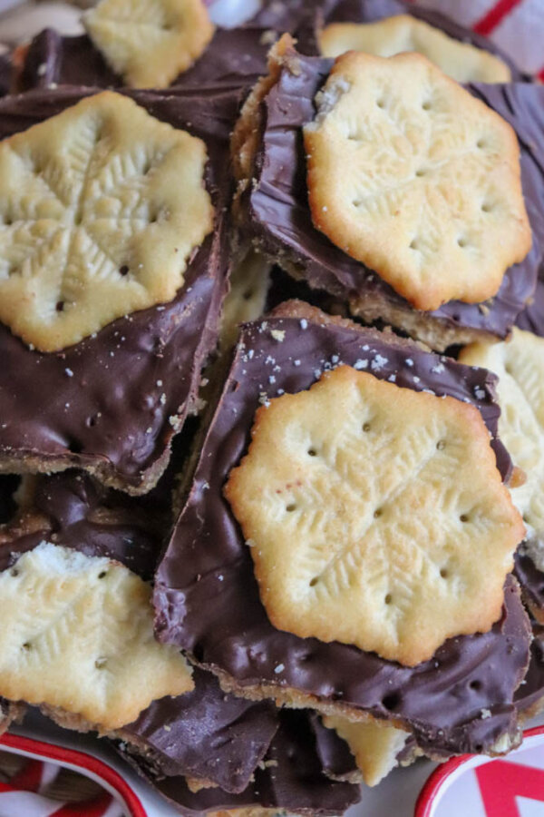 A close-up of stacked chocolate toffee bars topped with snowflake-patterned shortbread cookies, creating a festive holiday treat.