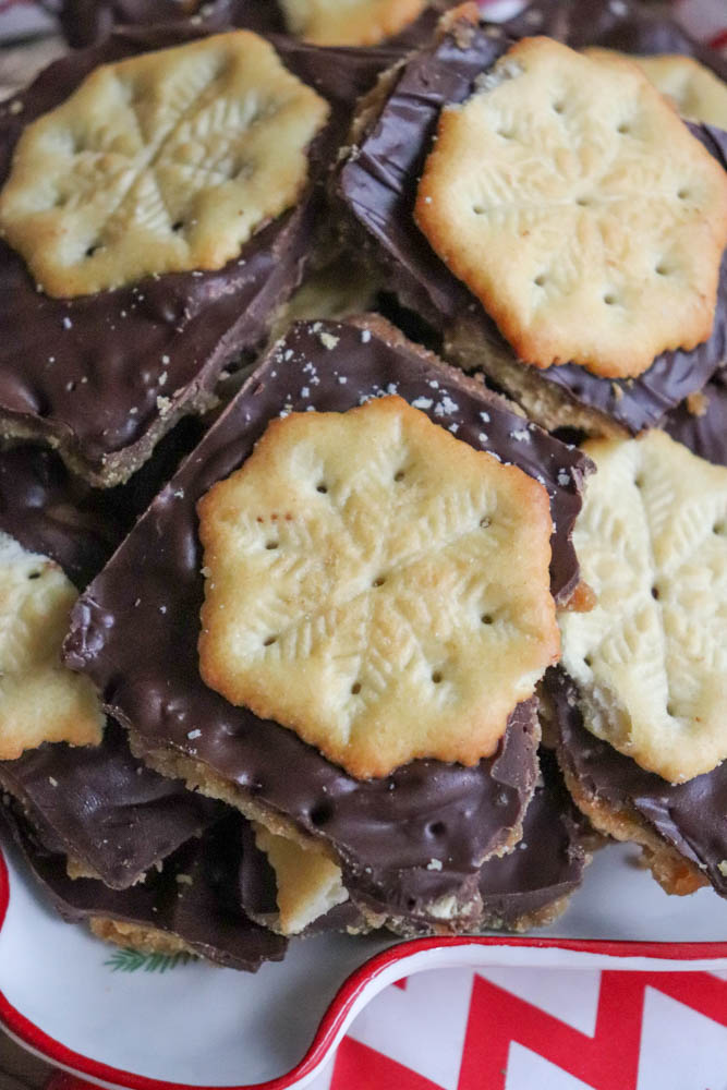 A plate of chocolate-covered crackers topped with snowflake-patterned cookies, arranged in a festive red and white dish.