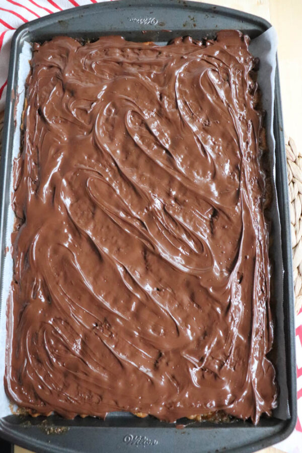 A rectangular baking tray filled with a dessert topped with a thick, glossy layer of melted chocolate, swirled evenly across the surface.