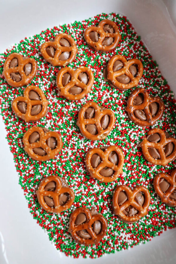 Small pretzels placed on a bed of red, white, and green sprinkles in a white dish, creating a festive holiday treat.