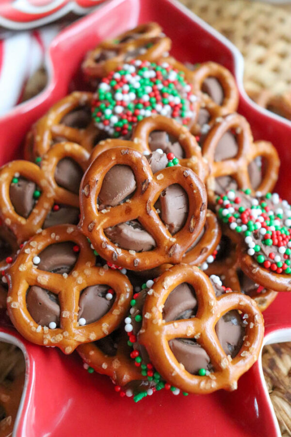 A festive plate filled with pretzels topped with melted chocolate and decorated with red, white, and green sprinkles, perfect for a holiday treat.