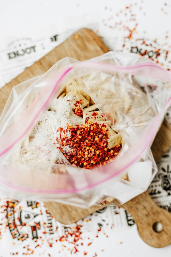 A ziplock bag filled with chopped tofu, flour, and red chili flakes, placed on a wooden cutting board with some chili flakes scattered around.