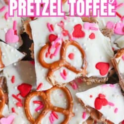A close-up of Valentineโs Day pretzel toffee topped with white chocolate, pretzels, red heart candies, and pink sprinkles. Text reads โValentineโs Day Pretzel Toffee SO GOOD!โ and homemadeheather.com at the bottom.