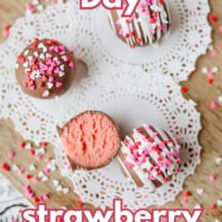 Three strawberry cake balls, one cut open to show the pink inside, are decorated with white and pink sprinkles and placed on a doily. Text reads Valentine’s Day strawberry cake balls.
