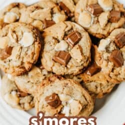 A plate of s’mores cookies topped with chocolate chunks and mini marshmallows sits on a red-checked cloth. Brown text reads the best s’mores cookies with homemadeheather.com at the bottom.