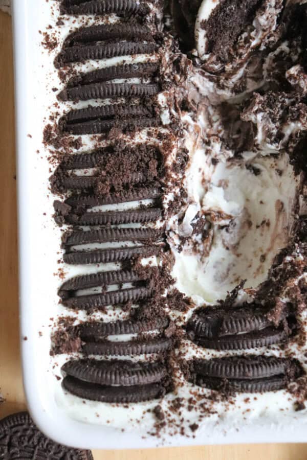 A close-up of a dessert dish filled with creamy ice cream and topped with whole and crushed chocolate sandwich cookies, partially scooped out on one side.