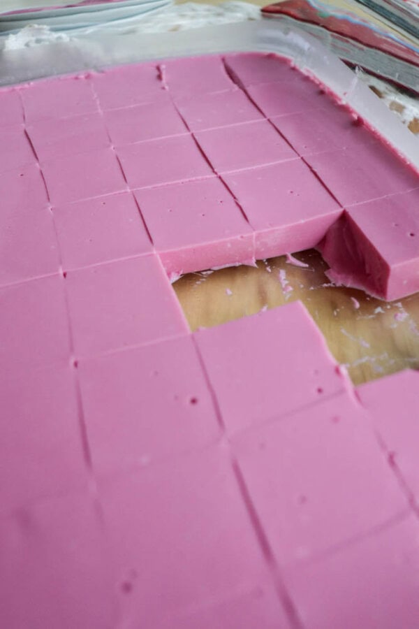 A tray of pink dessert cut into small squares, with one piece missing from the corner section. The surface is smooth and the texture appears creamy.