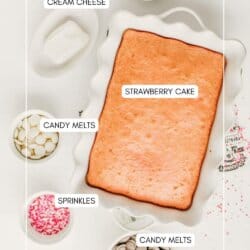 A baked rectangular strawberry cake in a white dish, surrounded by small bowls of cream cheese, oil, pink and white sprinkles, and white and milk chocolate candy melts. Ingredients are labeled.