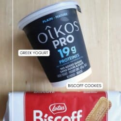 A container of Oikos Pro Greek yogurt and a package of Lotus Biscoff cookies are placed on a light wooden surface. Labels point to each item, identifying them as Greek yogurt and Biscoff cookies.