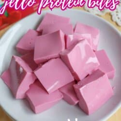 A white plate holds several pink, glossy, square-shaped jello protein bites. Text on the image reads 2-Ingredient Jello Protein Bites and SO GOOD! with a website link at the bottom.