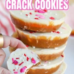 A hand holds a white chocolate-topped cookie with sprinkles, showing a bite taken out. Four more cookies are stacked in the background. Text reads Valentines Day Crack CookiesโSo Good!.