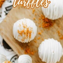 Three white chocolate-covered Biscoff cookie truffles are displayed on a wooden board, with one cut open to reveal a golden biscoff cookie butter delight filling. Crumbled cookies and whole cookies surround them. Text reads: “Biscoff Cookie Truffles.”.