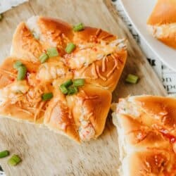 A wooden cutting board holds crab rangoon sliders topped with melted cheese and chopped green onions. Partially sliced rolls reveal a creamy filling. Text reads “Crab Rangoon Sliders” and “homemadeheather.com.”.