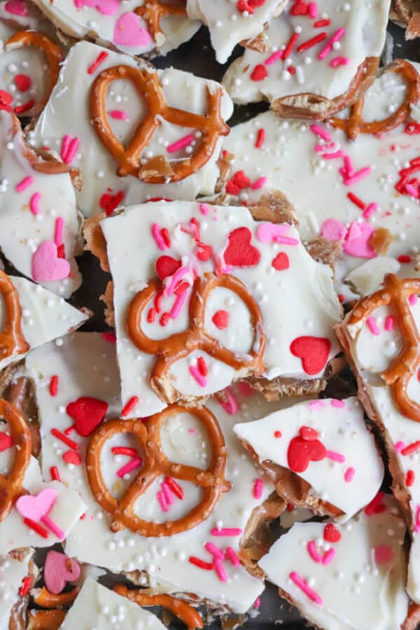 White chocolate bark topped with pretzels, heart-shaped sprinkles, pink and red confetti sprinkles, and white sugar pearls, broken into pieces and arranged closely together.