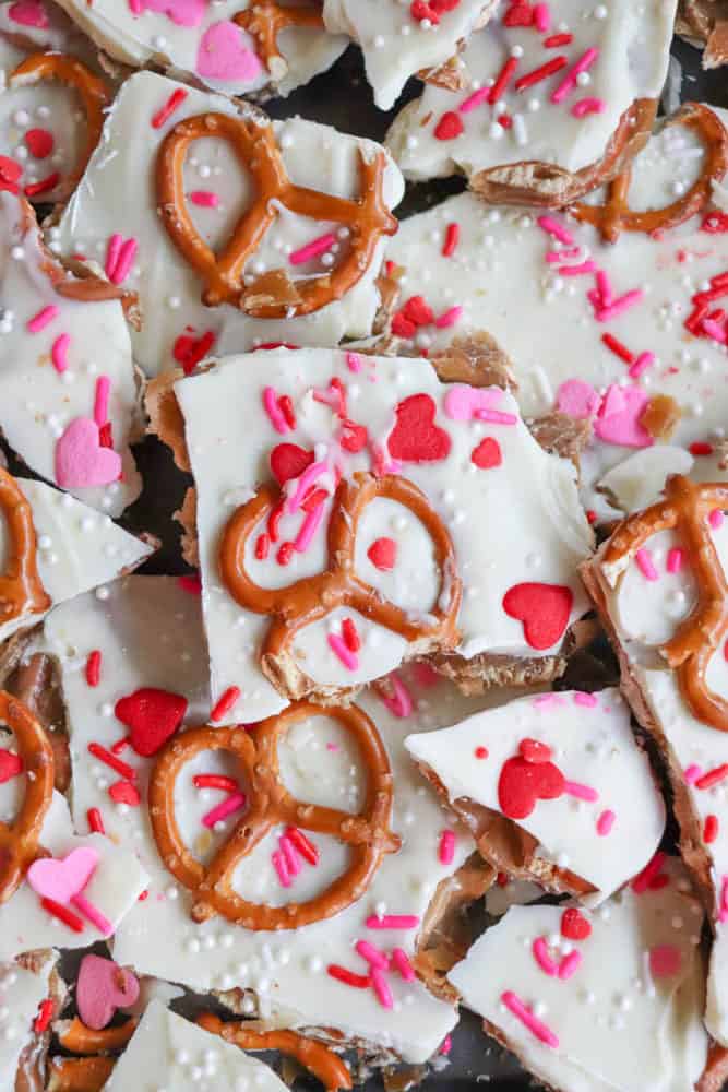 White chocolate bark topped with pretzels, heart-shaped sprinkles, pink and red confetti sprinkles, and white sugar pearls, broken into pieces and arranged closely together.