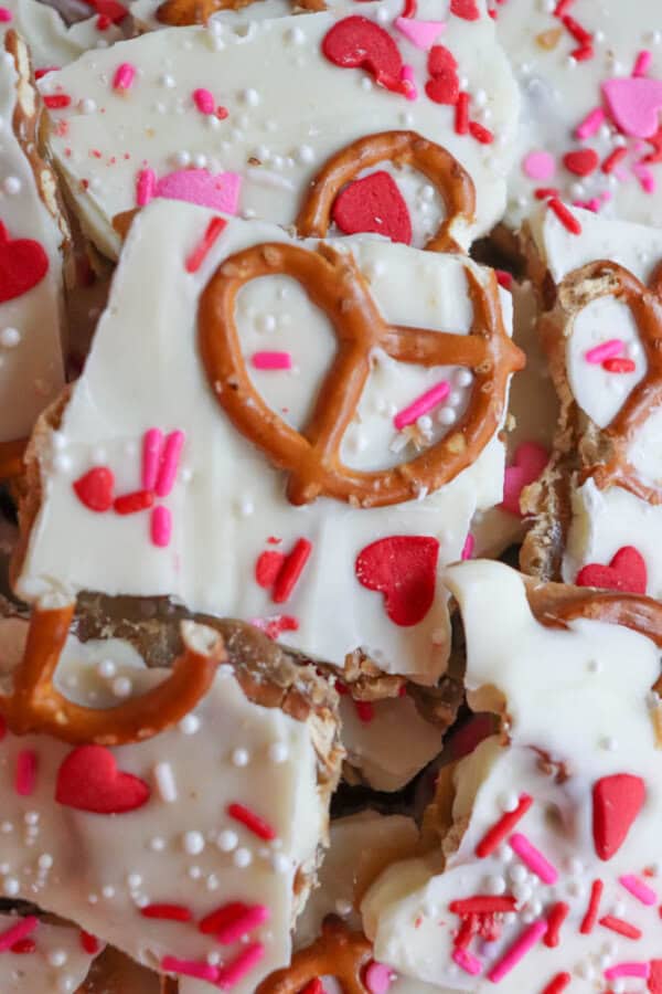 A close-up of white chocolate bark topped with pretzels, red and pink heart-shaped sprinkles, and white nonpareils, creating a festive and colorful treat.