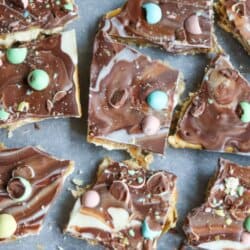 Overhead view of chocolate toffee topped with pastel mini egg candies, broken into squares on a baking sheet. The text reads: Mini Egg Cracker Toffee and homemadeheather.com at the bottom.