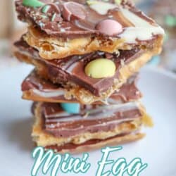 A stack of chocolate toffee bark topped with colorful candy mini eggs is displayed on a white plate. Text on the image reads Mini Egg Cracker Toffee and homemadeheather.com at the bottom.