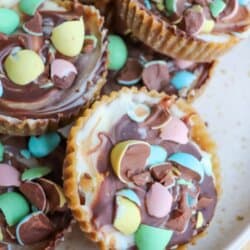 A plate of mini egg crack cookies topped with colorful chocolate candy eggs and a drizzle of chocolate, arranged in cupcake wrappers. Text on the image reads Mini Egg Crack Cookies and homemadeheather.com.
