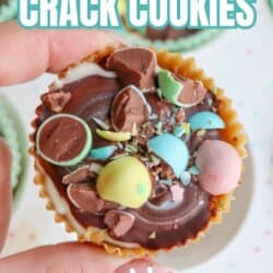 A hand holding a round cookie topped with chocolate and colorful mini egg candy pieces. Text on image reads Mini Egg Crack Cookies and So Easy. Website: homemadeheather.com.