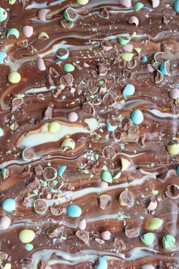 Swirled milk and white chocolate bark topped with colorful pastel candy-coated chocolate pieces and chocolate chips, creating a marbled and festive appearance.