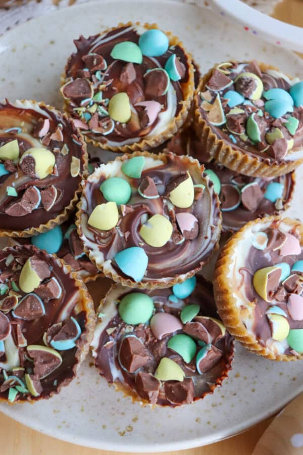 A plate of chocolate swirled cupcakes topped with crushed pastel-colored candy eggs and chocolate pieces, arranged closely together.