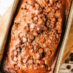 A loaf of chocolate zucchini bread topped with chocolate chips sits in a baking pan. The text above reads “chocolate zucchini bread,” and the website homemadeheather.com is displayed at the bottom.