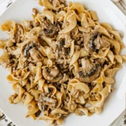 A white plate filled with beef, mushrooms, and egg noodles sits on a table. The image has text that reads: Beef & Mushroom one pot noodles and homemadeheather.com at the bottom.