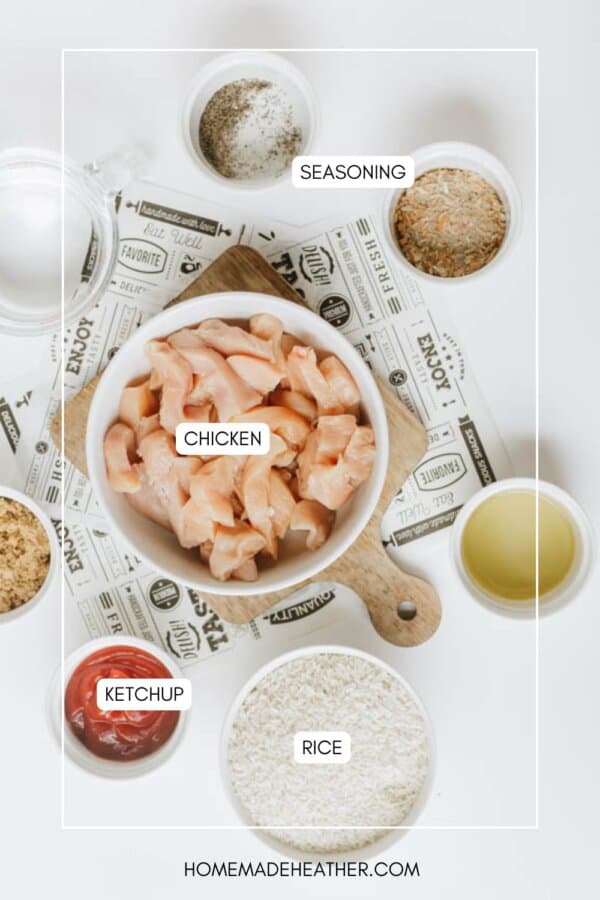 Overhead view of raw diced chicken in a bowl, surrounded by small bowls with ketchup, rice, oil, spices, and seasonings on a white surface. Labels identify each ingredient.