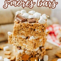 Three stacked s’mores bars made with Golden Grahams cereal, mini marshmallows, and chocolate pieces, with more cereal and marshmallows scattered around. Text reads: Golden Graham s’mores bars. So good!.