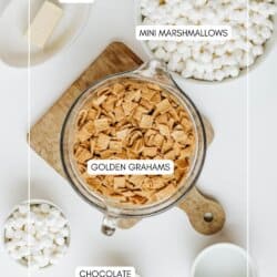 Top-down view of ingredients on a white table: a bowl of mini marshmallows, a bowl of Golden Grahams cereal, a cup with chocolate pieces, a stick of butter on a wooden board, and a cup of milk. Labels identify each item.
