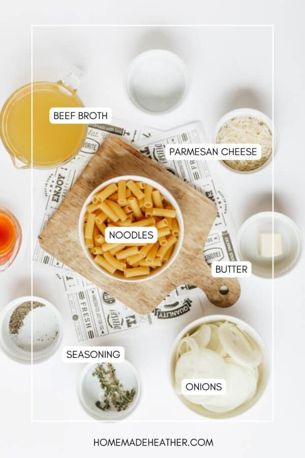 Top-down view of ingredients for a pasta dish, including beef broth, parmesan cheese, dry noodles, butter, sliced onions, seasonings, and herbs, each labeled and arranged on a white surface with a wooden board.