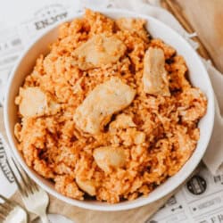 A white bowl filled with one pot sweet & savory chicken and rice sits on a wooden board, with a fork and spoon nearby and a napkin in the background.