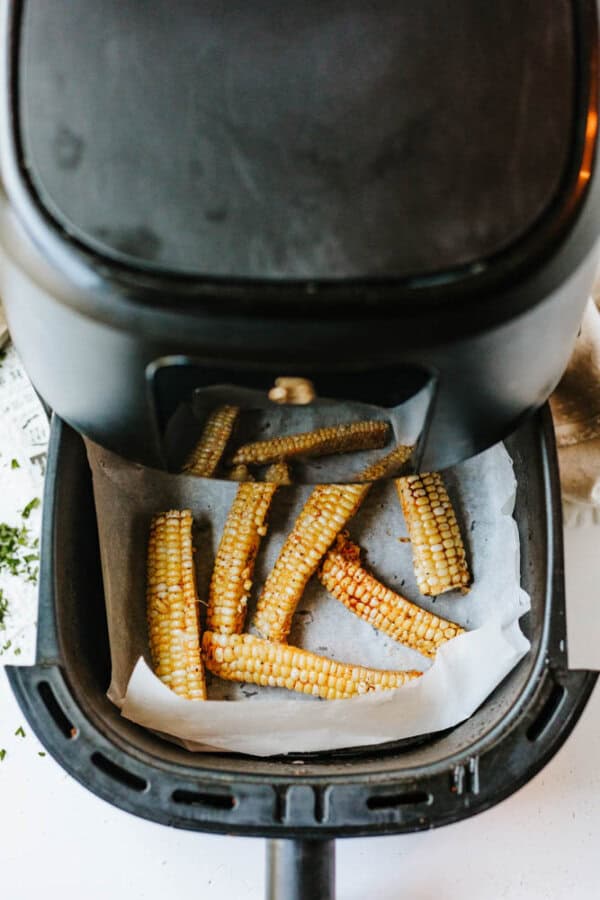 Corn ribs arranged on parchment paper inside an open air fryer basket, with the air fryer lid partially visible at the top of the image.